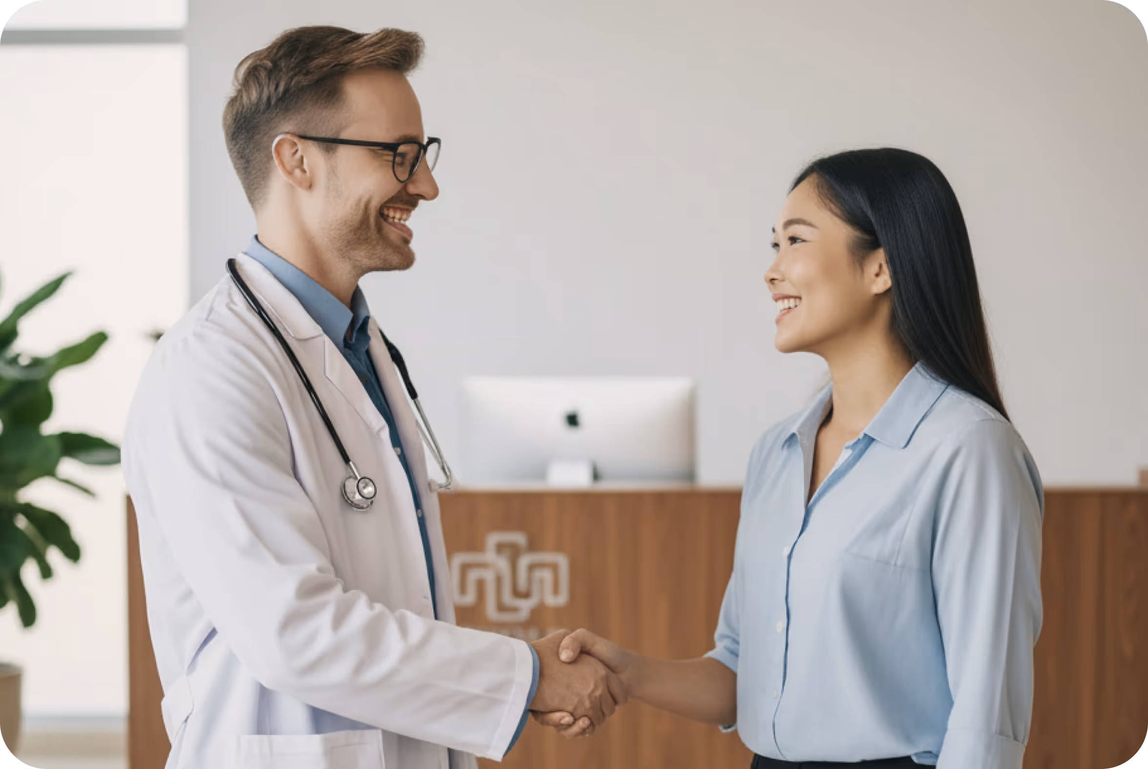 Male doctor wearing a white coat and stethoscope shaking hands with female patient in a medical office.