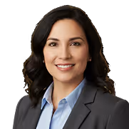 Smiling woman with dark hair wearing a gray blazer and light blue collared shirt against a white background.
