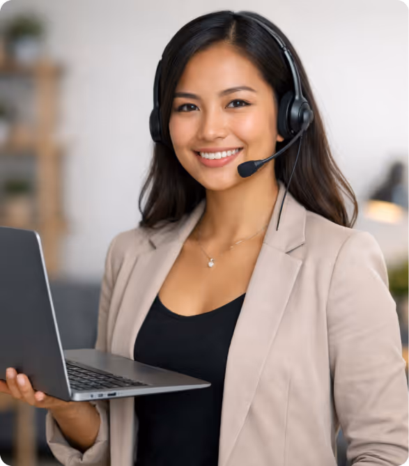 Smiling woman wearing headset and beige blazer holding an open laptop in a bright office.