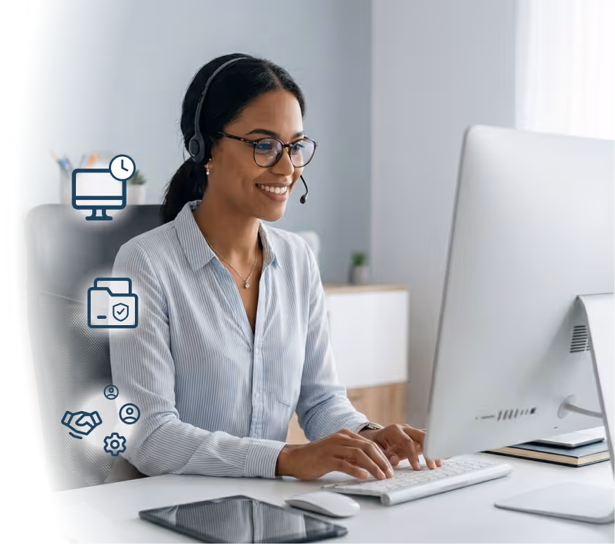Smiling woman wearing glasses and a headset typing on a keyboard in front of a desktop computer at a desk with a tablet and mouse.