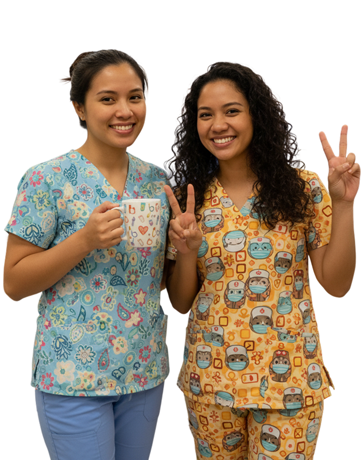 Two smiling women wearing colorful medical scrubs, one holding a mug and the other showing peace signs with both hands.