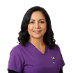 Smiling woman with dark curly hair wearing a purple medical scrub top with a stethoscope emblem.