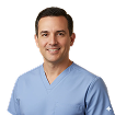 Smiling man wearing light blue medical scrubs against a white background.
