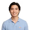 Smiling young man with black hair wearing a light blue polo shirt against a white background.