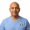 Smiling middle-aged man wearing light blue scrubs with a small Mexican flag patch on the chest pocket.