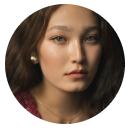 Portrait of a young woman with long brown hair and pearl earrings, wearing a maroon top.