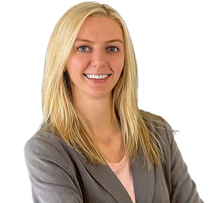 Smiling blonde woman wearing a navy blazer and gold necklace against a transparent background.