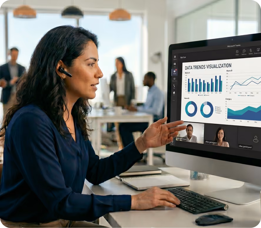 Woman with headset pointing at data trends visualization graphs during a video call on a desktop in an office.
