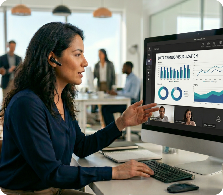 Woman with headset pointing at data trends visualization graphs during a video call on a desktop in an office.