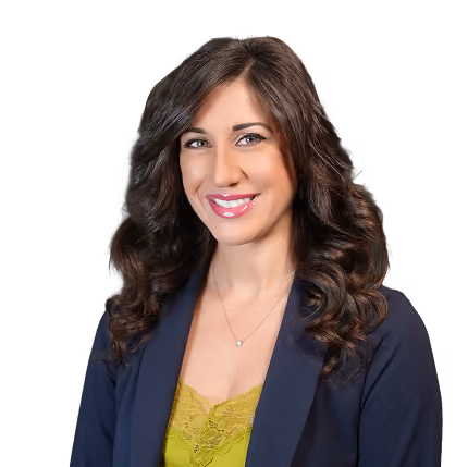 Woman with long curly brown hair wearing a navy blazer and green lace top smiling at the camera.