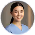 Smiling young woman with dark hair wearing light blue scrubs against a neutral background.