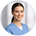 Smiling female healthcare worker with dark hair in light blue scrubs on blurred background.