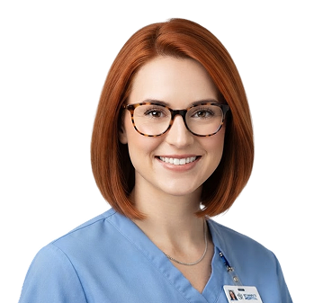 Smiling woman with red hair wearing tortoiseshell glasses and light blue medical scrubs with a name badge.