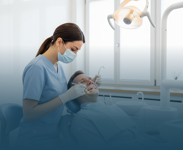 Female dentist wearing a mask and gloves examining a male patient’s teeth with dental tools in a bright dental office.