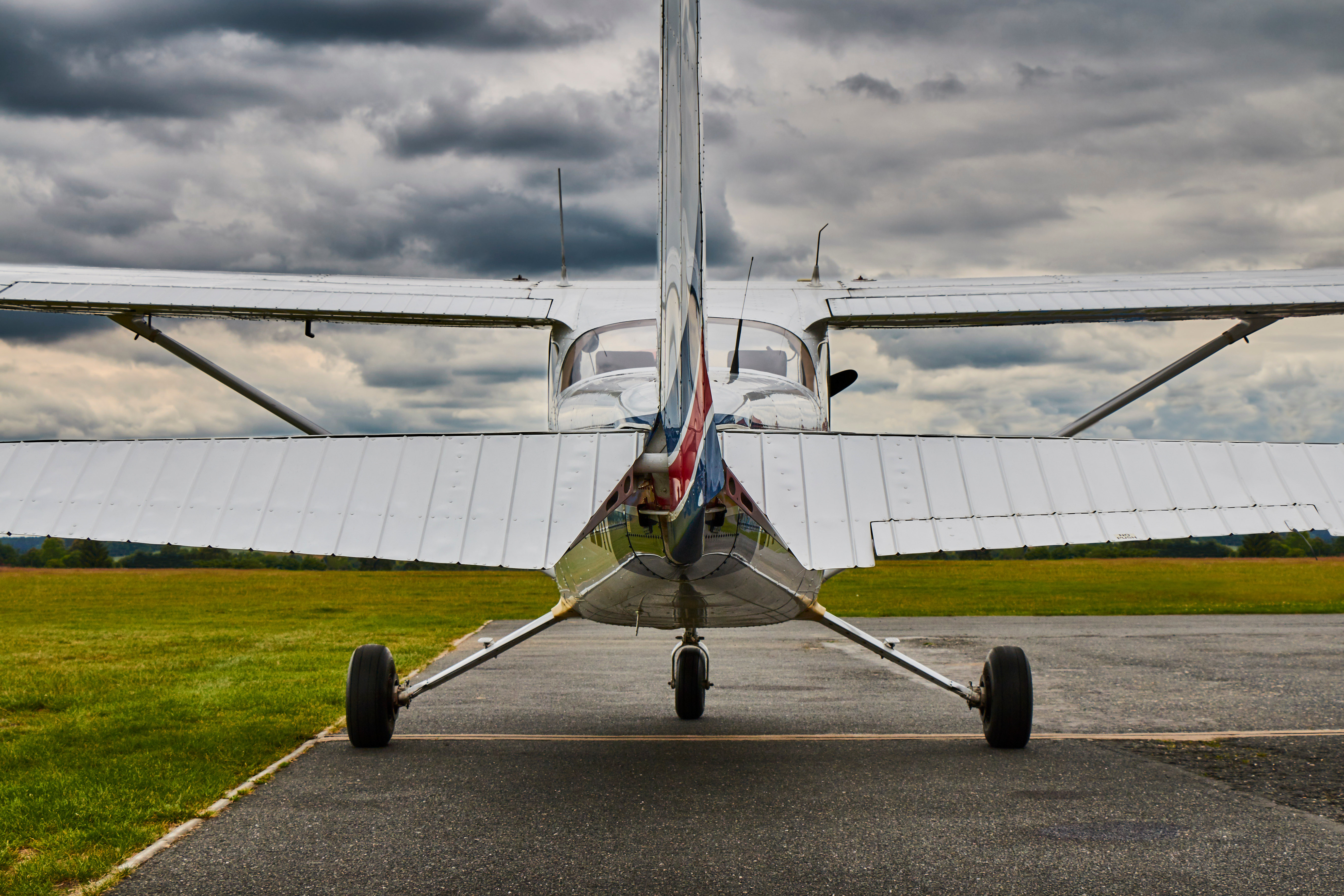 Rear view of a small white airplane parked on an asphalt runway with green grass and cloudy sky in the background.