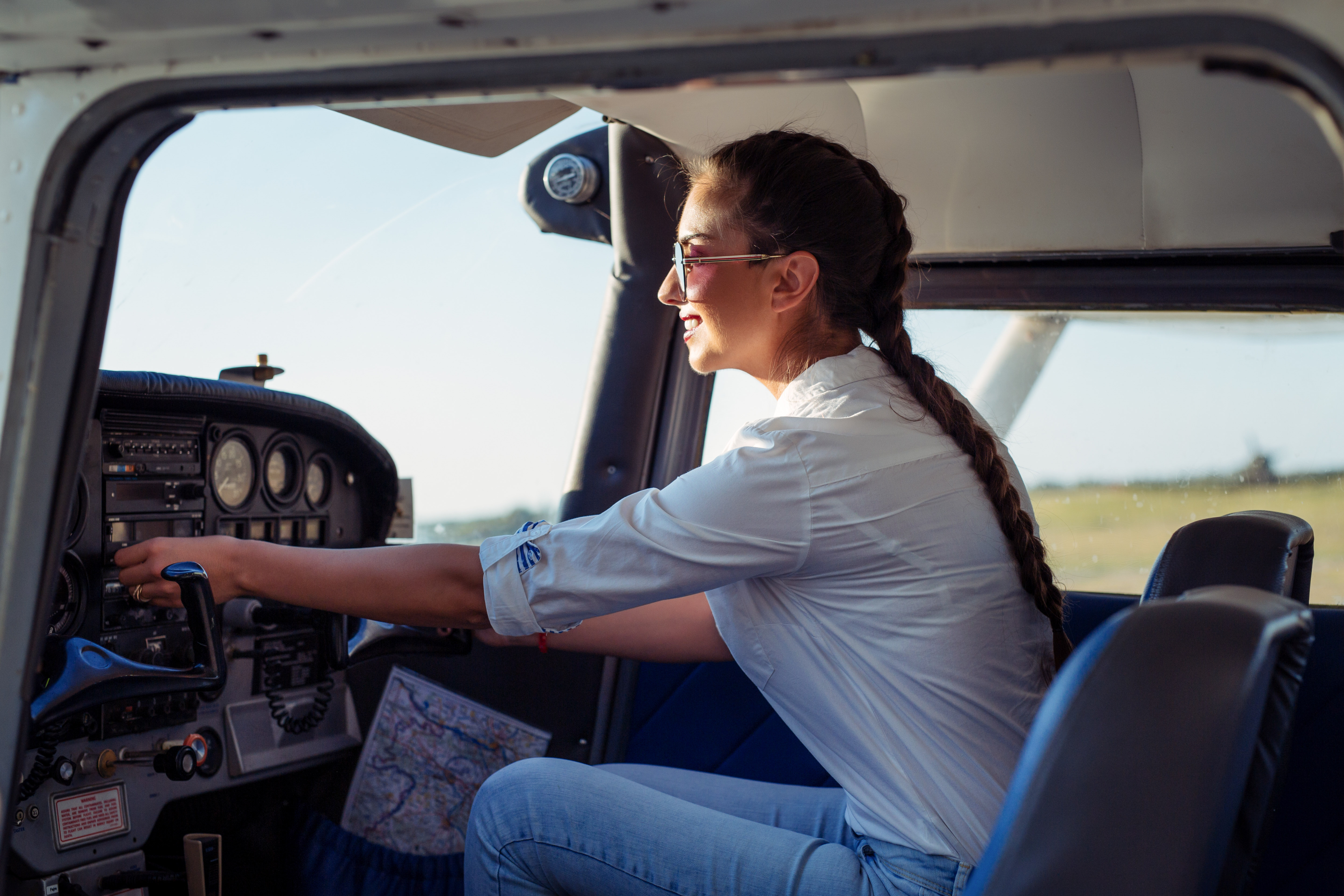 Woman with a long braided ponytail adjusting controls inside a small airplane cockpit.