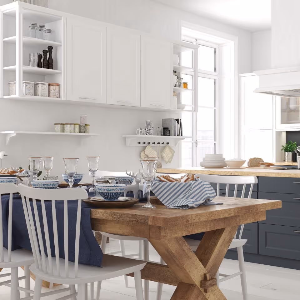 Lyst og moderne kjøkken med hvite skap, et spisebord i tre og blå tekstiler.