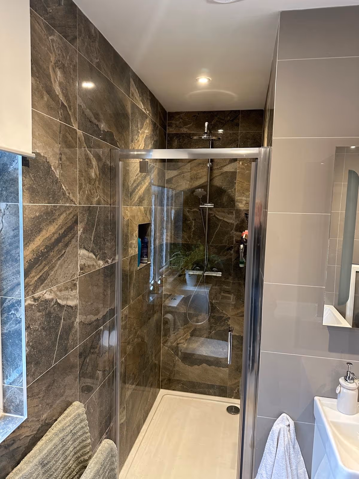 Modern bathroom shower with dark marble tiles, glass door, and overhead showerhead.