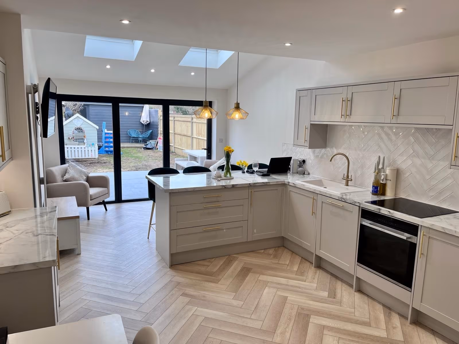 Modern kitchen with marble countertops, L-shaped cabinets, two pendant lights, and glass doors opening to a backyard.