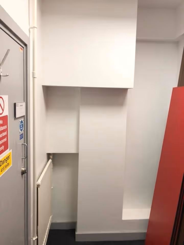 Small empty corner room with gray door, white radiator, and a red panel against the wall.