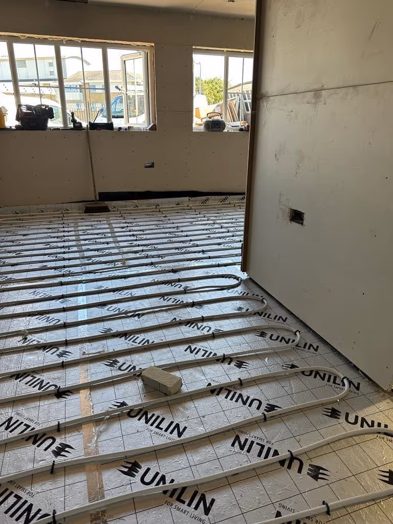 Indoor underfloor heating pipes being installed on insulation boards with 'UNILIN' branding in a room under construction.