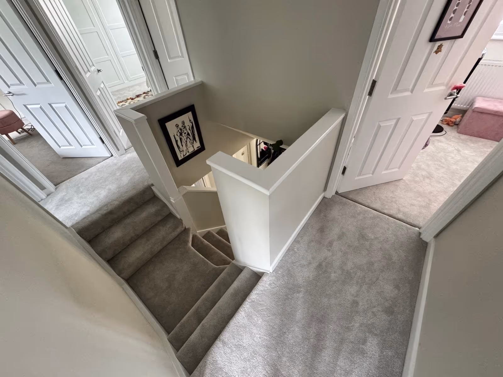 Top view of a carpeted staircase and hallway with white walls and open doors leading to adjacent rooms.