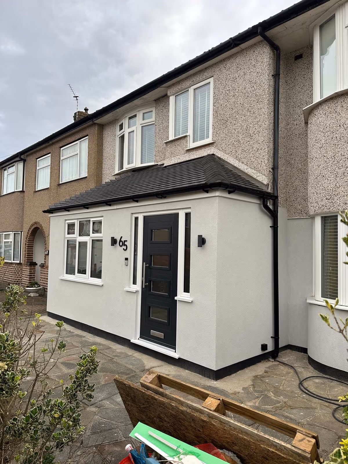 Front view of a two-story row house with a black door, white walls, and the house number 65 displayed next to the entrance.