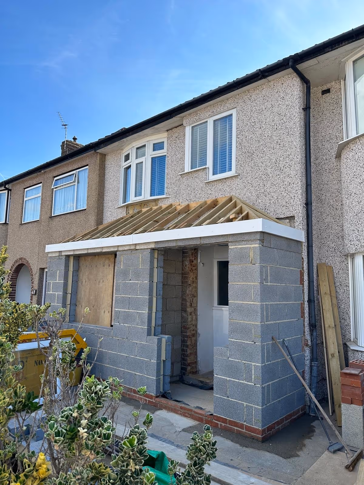 Residential house with an under-construction porch extension made of gray concrete blocks and wooden roof framing.