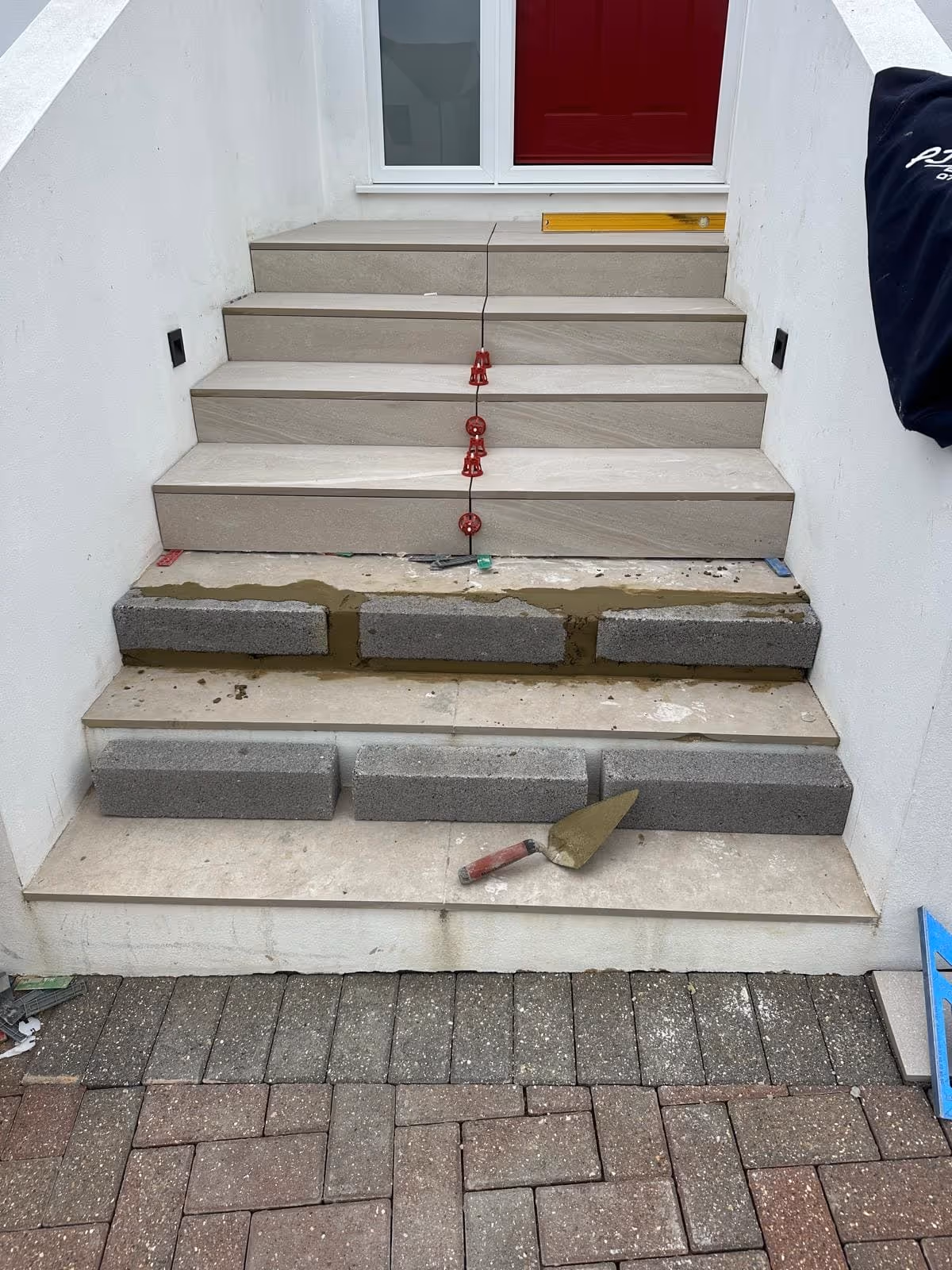 Outdoor stairs under construction with some steps tiled and concrete blocks and trowel placed on unfinished steps.