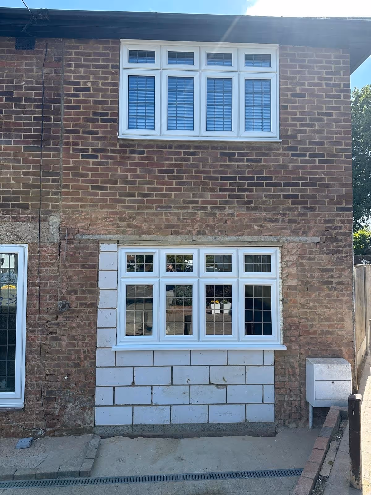 Two white-framed windows on a brick house, with new lower window surrounded by unfinished blockwork.