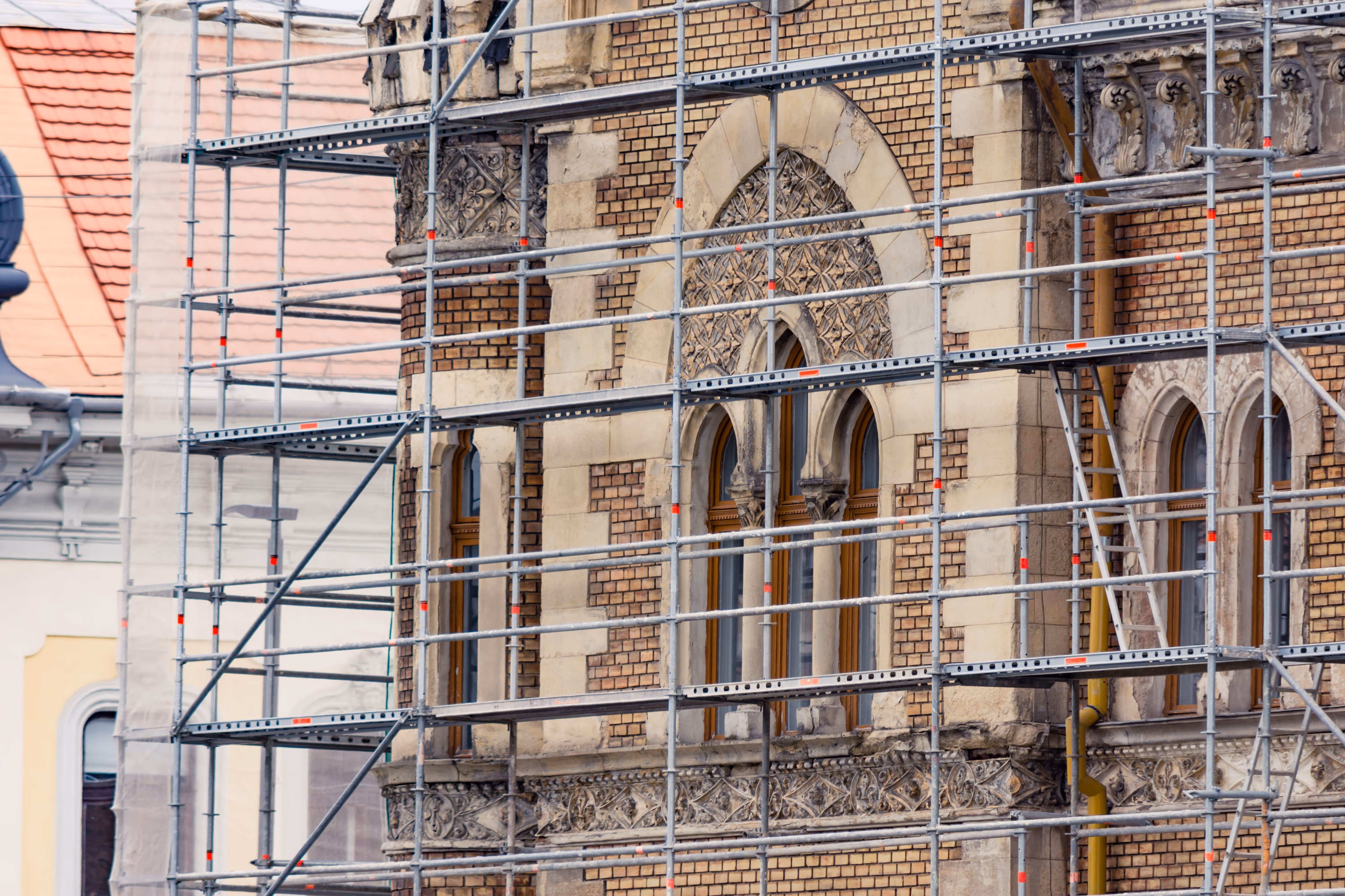 Close-up of historic brick building facade with ornate arched windows and detailed stonework under metal scaffolding.