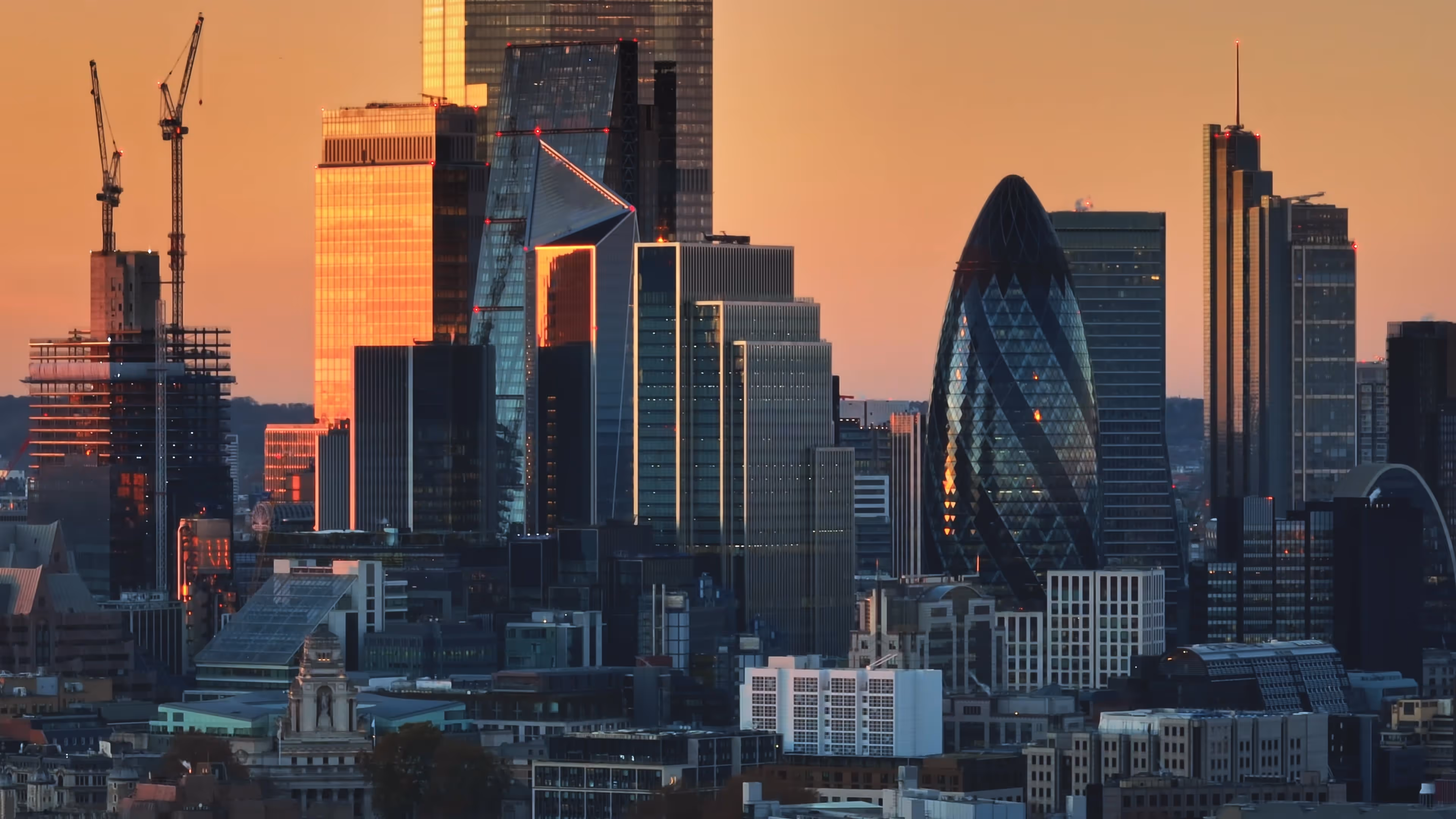 London city skyline at sunset featuring the Gherkin and modern skyscrapers reflecting golden light.