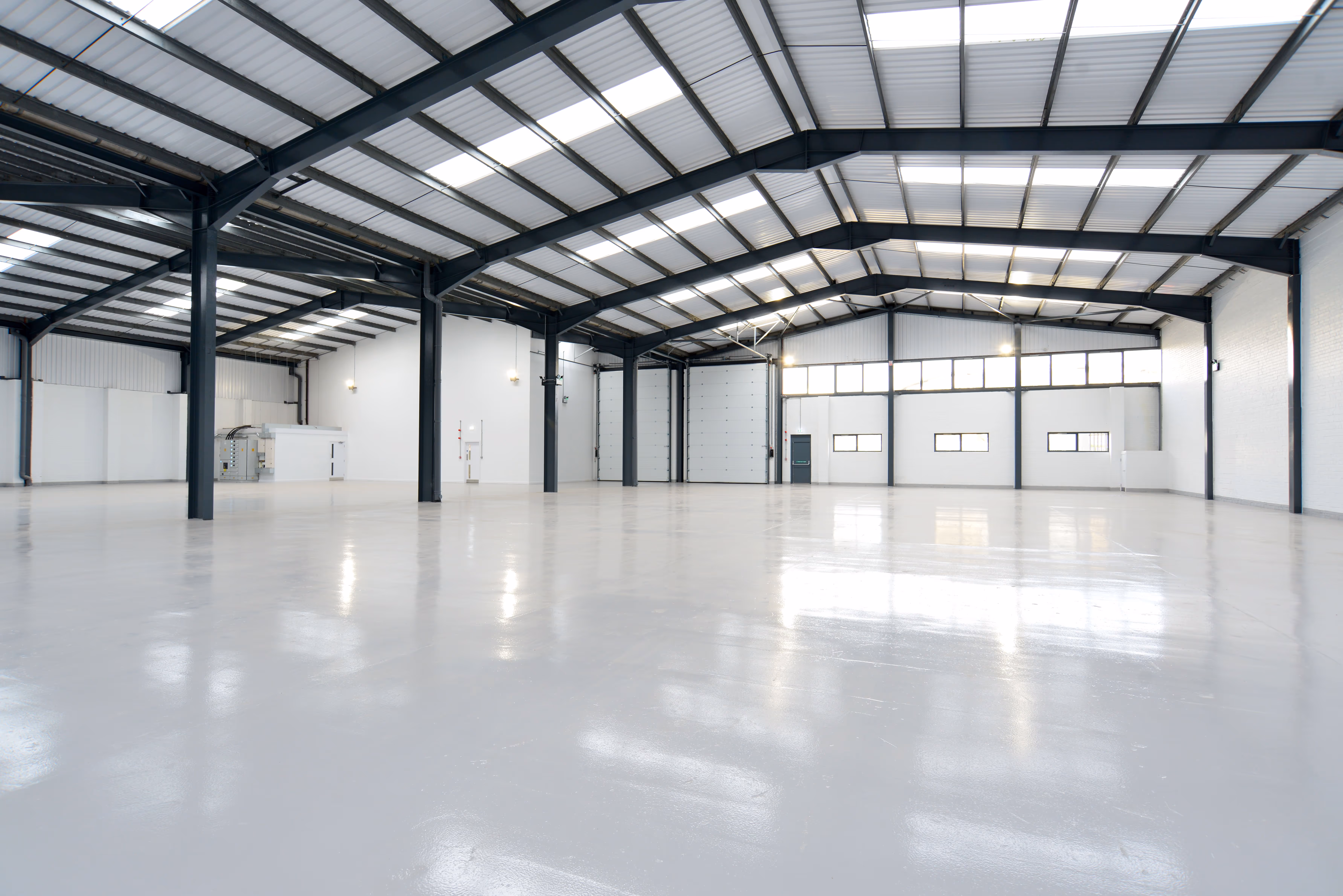 Spacious empty industrial warehouse with polished concrete floor, white walls, and metal roof beams.