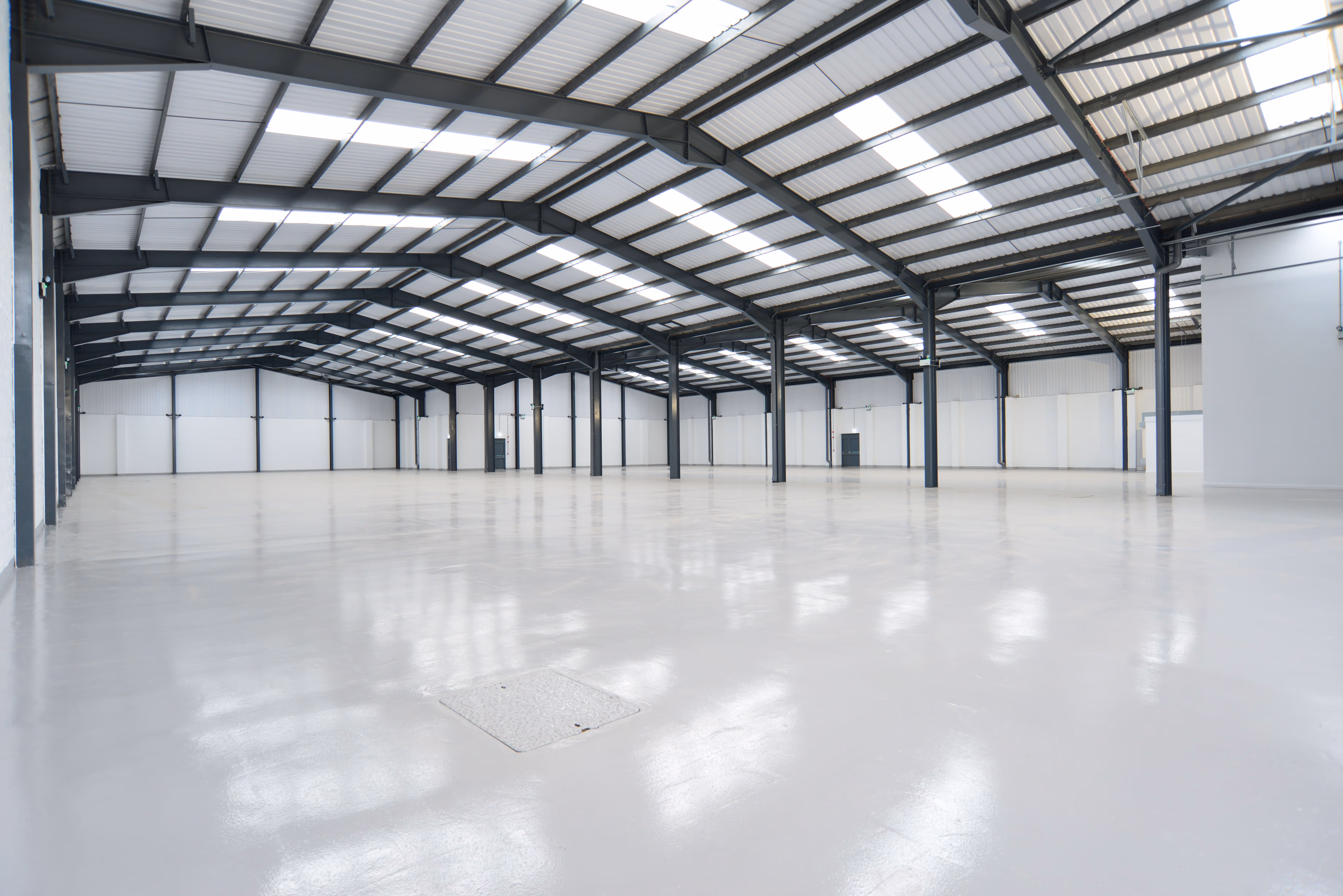 Large empty industrial warehouse with white polished floor and black steel support beams.