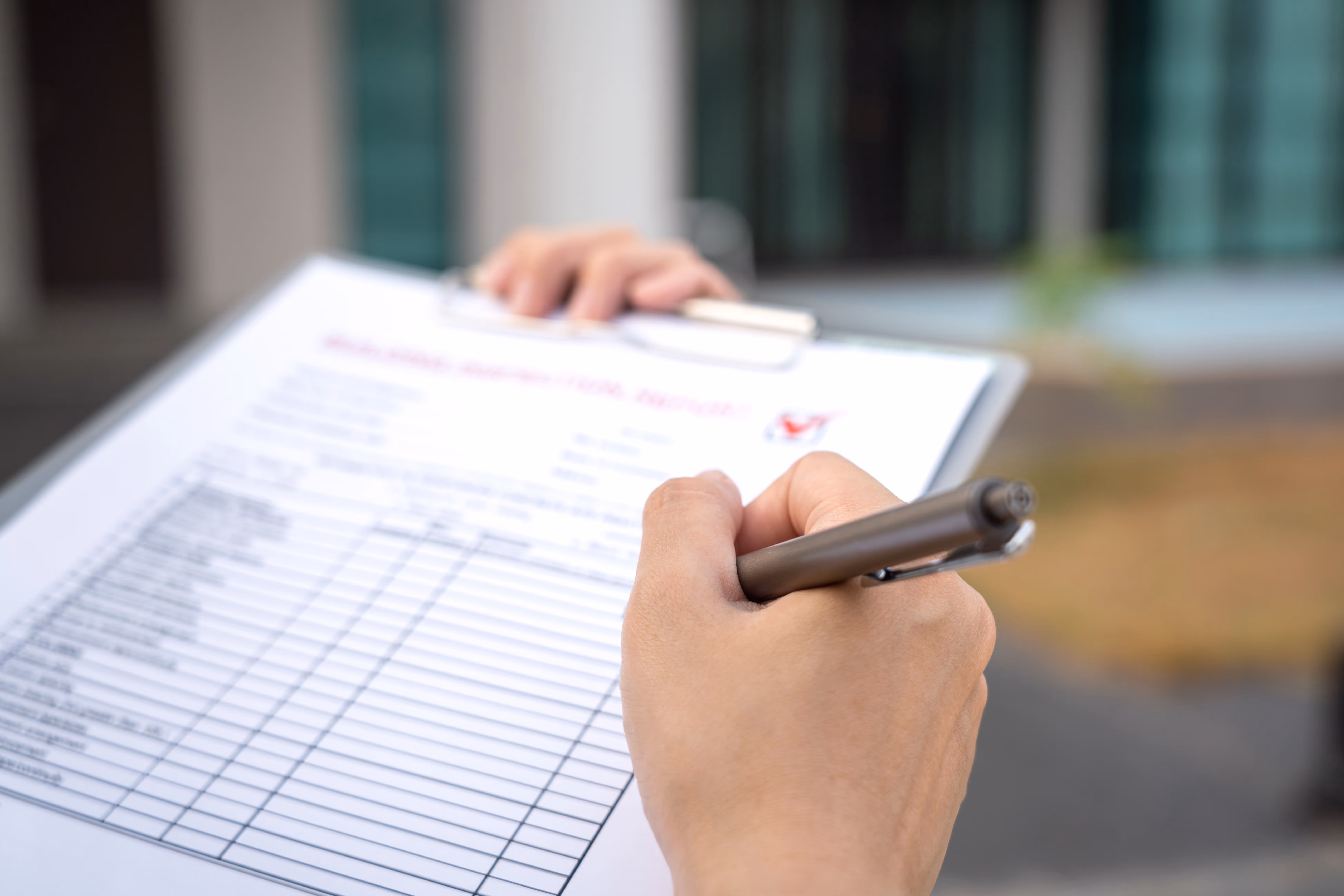 Hand holding a pen and writing on a checklist inspection form on a clipboard.