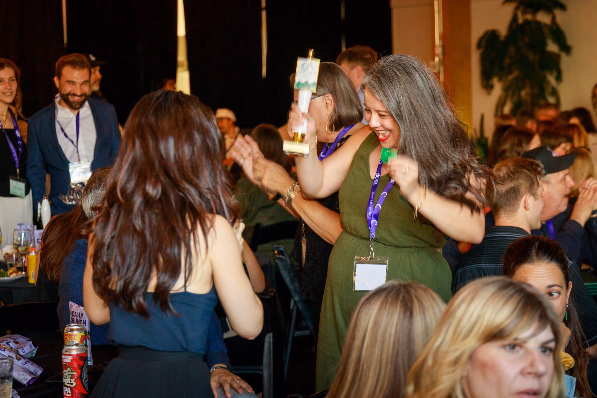 Group of people celebrating indoors, one woman in green dress holding a trophy and smiling.