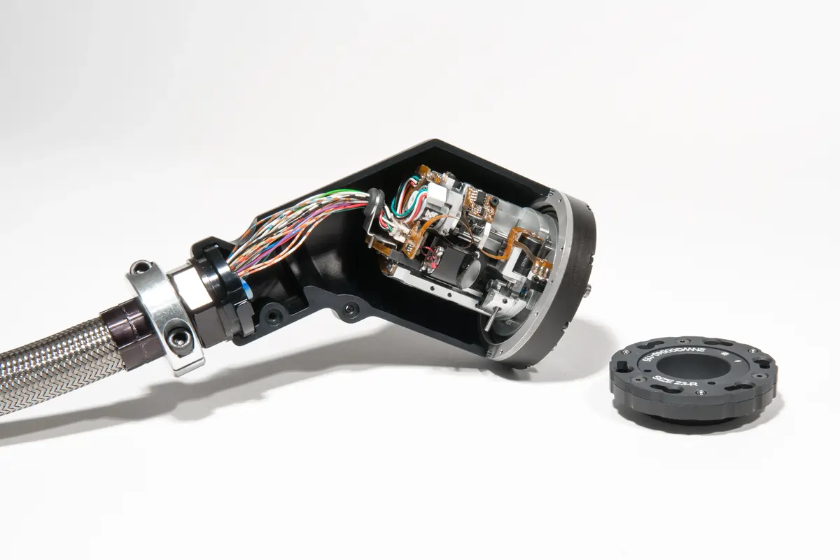 Opened electronic device with visible colored wires and circuit components beside a separate circular black cover labeled 'SIZE 23-R'.