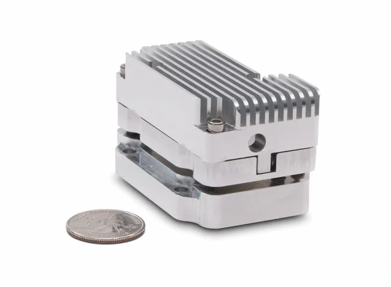 Compact silver metal heat sink with fins next to a quarter for size comparison.