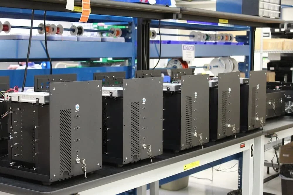 Row of black electronic server units with ventilation holes and locks on a laboratory workbench.