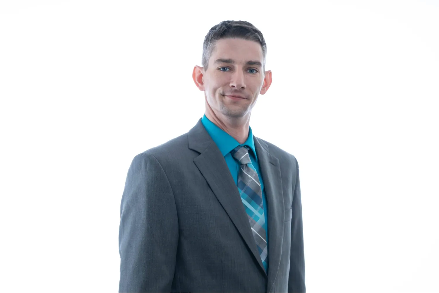 Man wearing a gray suit with a teal shirt and patterned tie, smiling slightly against a white background.