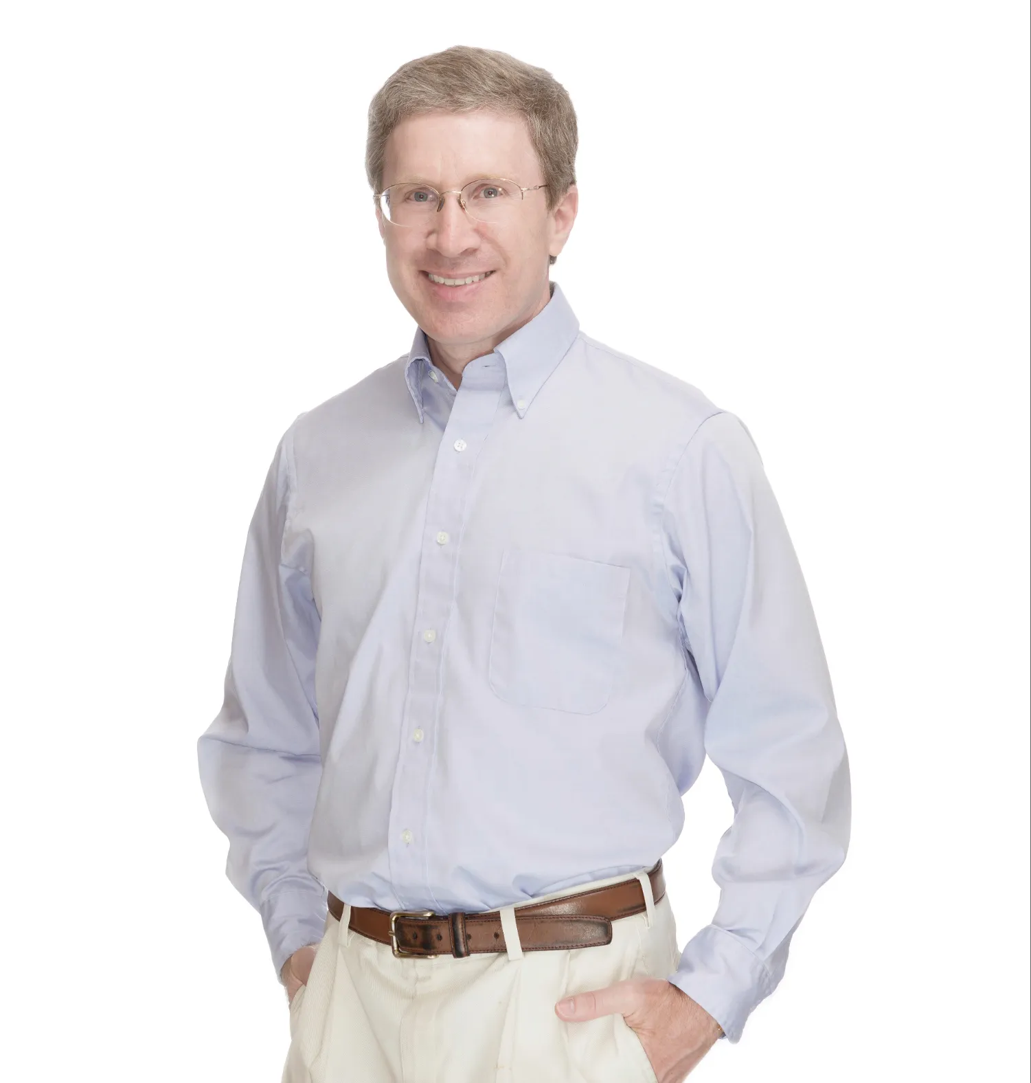 Smiling man with glasses wearing a light blue button-up shirt and beige pants with hands in pockets.