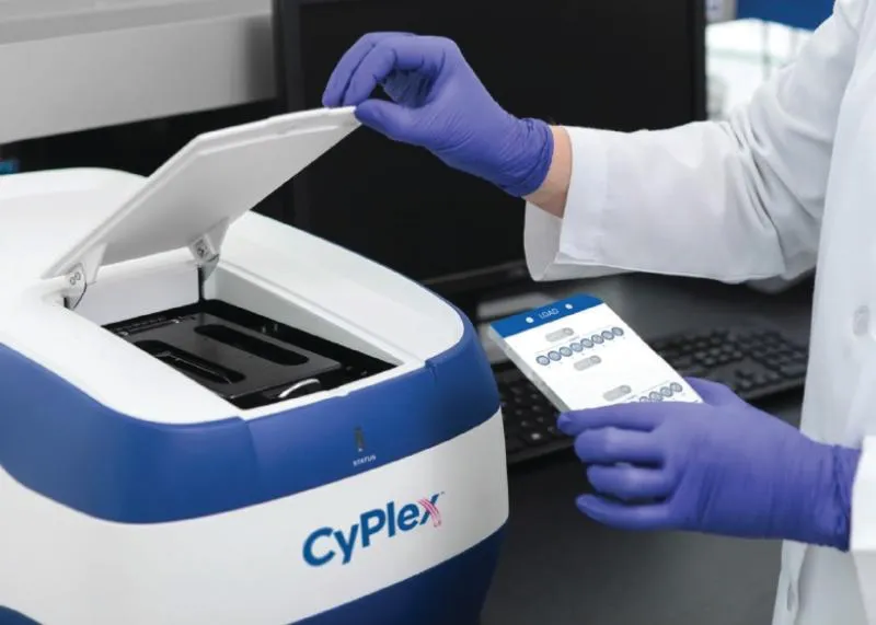 Person wearing purple gloves opening a CyPlex branded laboratory device while holding a test tray with sample slots.