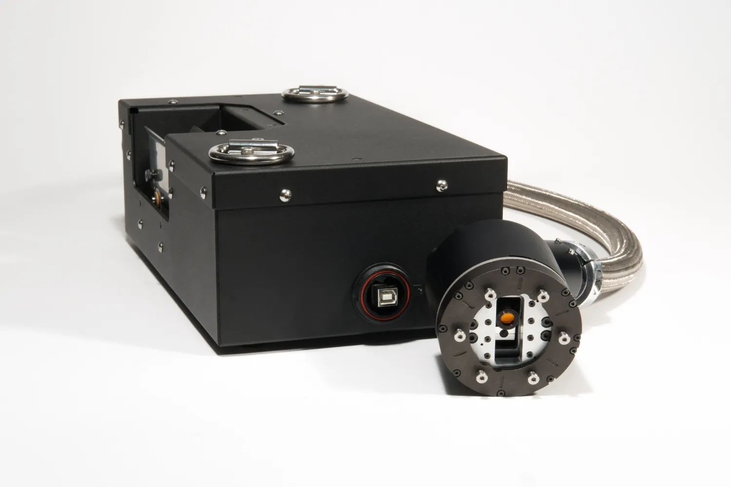 Black rectangular device with metal rings on top and a cylindrical component connected by a braided cable.