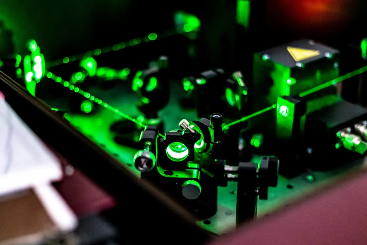 Laser optics setup with green laser beams passing through lenses and mirrors on an optical table.