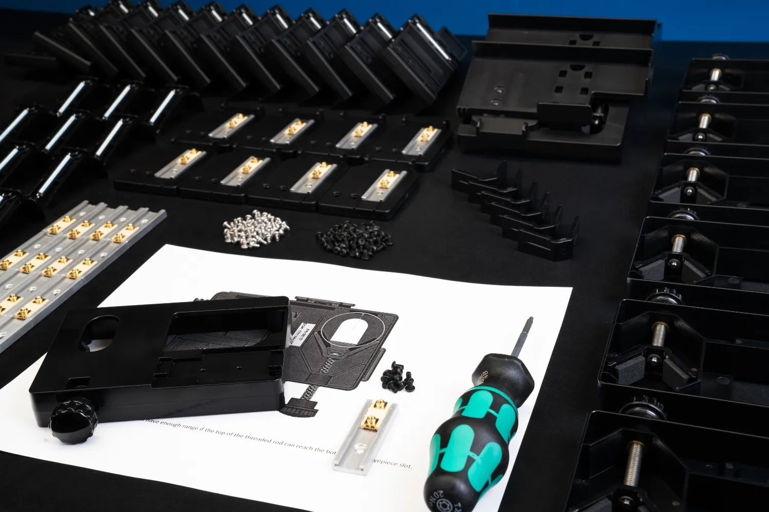 Assembly components and a screwdriver arranged on a black surface, including plastic parts, screws, metal connectors, and a printed instruction sheet.