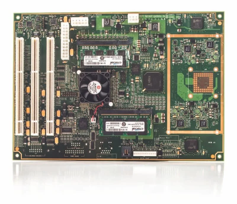 Green printed circuit board with multiple integrated circuits, RAM modules, connectors, and a small cooling fan.