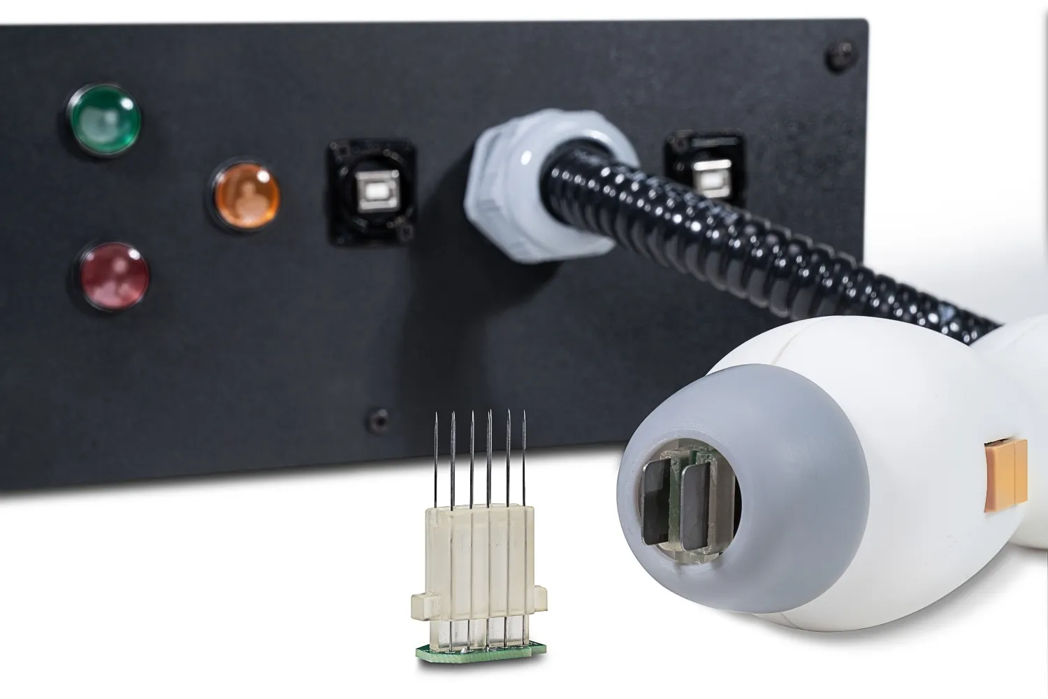 Close-up of a black control panel with multi-colored indicator lights, connected to a white handheld device with a gray tip and a small removable component with five thin metal needles.