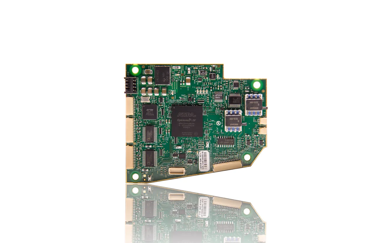 Rectangular green circuit board with multiple integrated chips and electronic components, reflected on a shiny white surface.