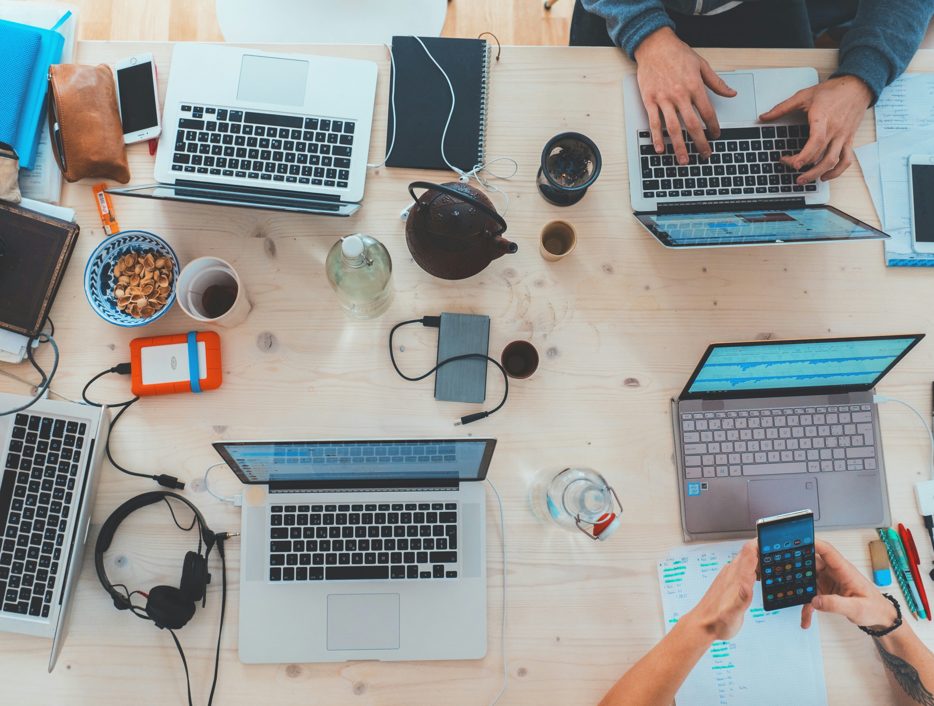 An image top down of a table surface with computers set up and hands typing and working.