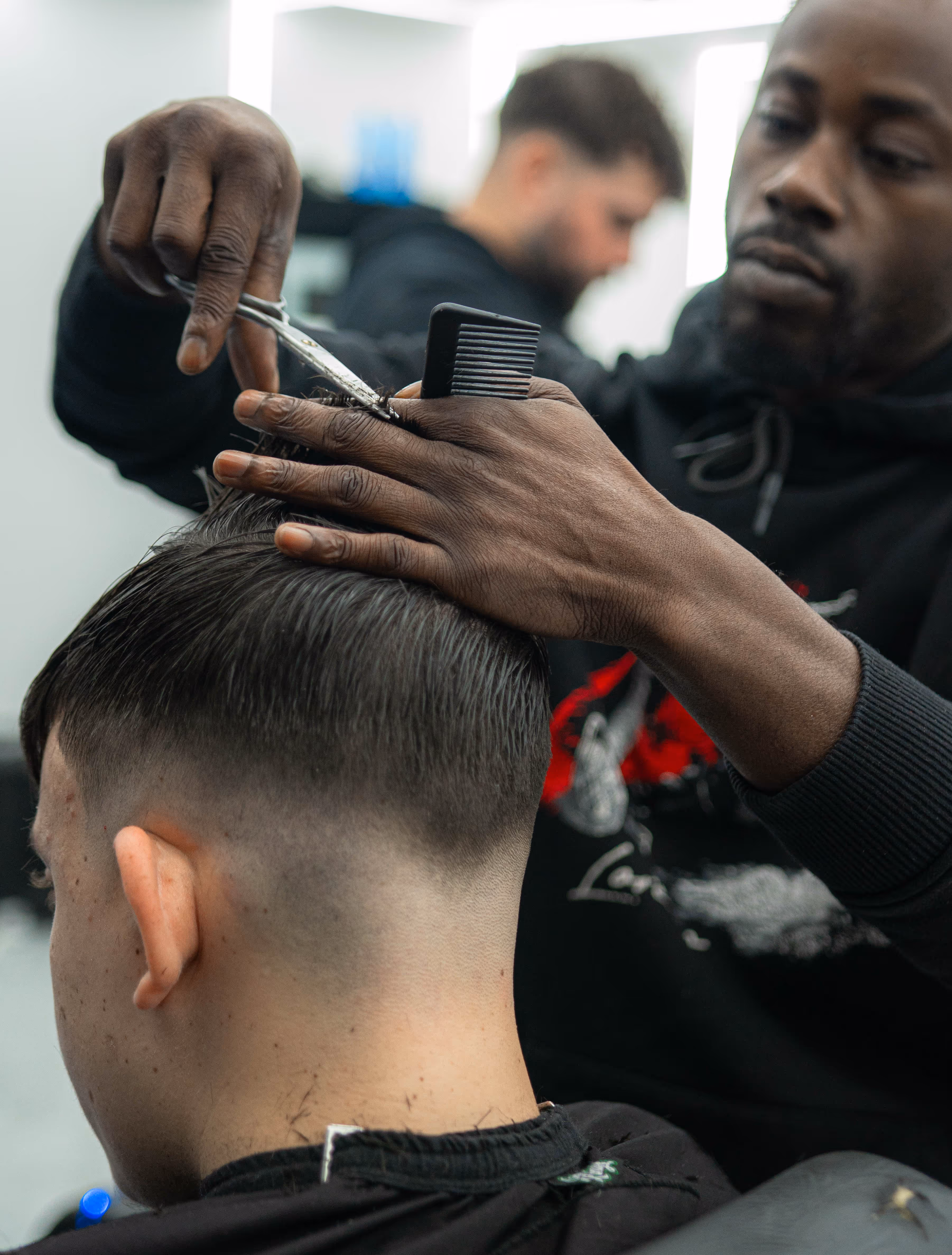 Barber trimming the hair on the back of a male client's head with scissors and a comb.